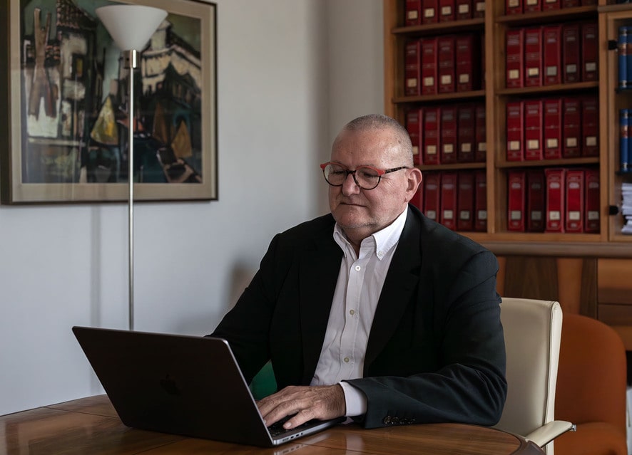 foto dell'Avvocato Piero Gallimberti seduto davanti ad un computer portatile con alle spalle una libreria che guarda il computer